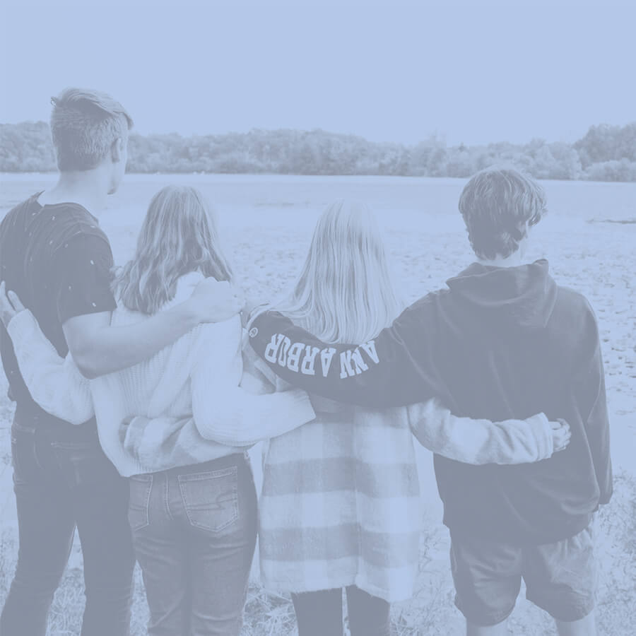A group of students embrace, shoulder to shoulder, as they glance across the Huron River.