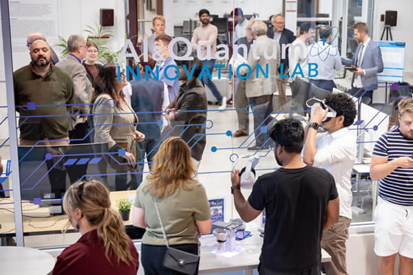 Guests explore the CUW AI & Quantum Innovation Lab during the November 5, 2025 pitch event, viewed through a glass wall labeled 'AI & Quantum Innovation Lab.' Some participants interact with technology and VR devices.