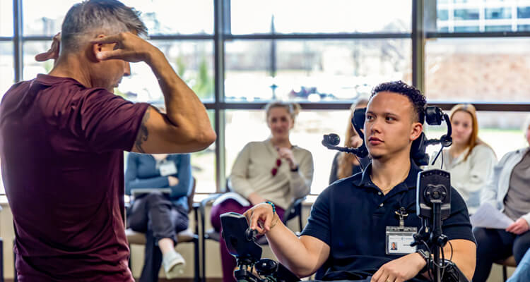Students at Concordia University Wisconsin’s Interdisciplinary Clinic watch as a classmate tries out a specialized wheelchair. The group gathers around, observing closely and asking questions, while an instructor guides the hands-on learning experience.