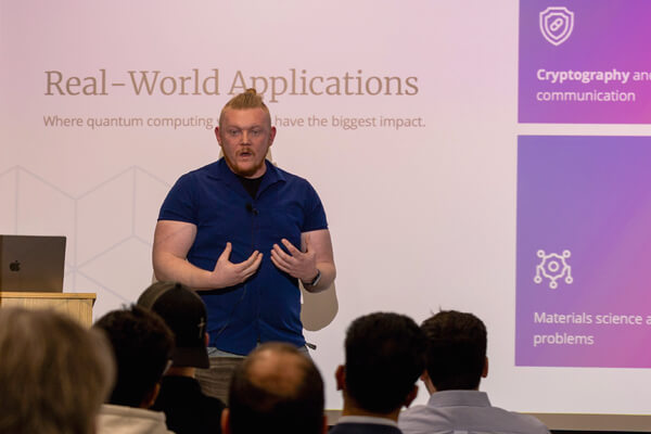 A presenter at Concordia University Wisconsin's AI & Quantum Innovation Lab (K. Harrington) discussing real-world applications of quantum computing, such as cryptography and materials science, with an audience.
